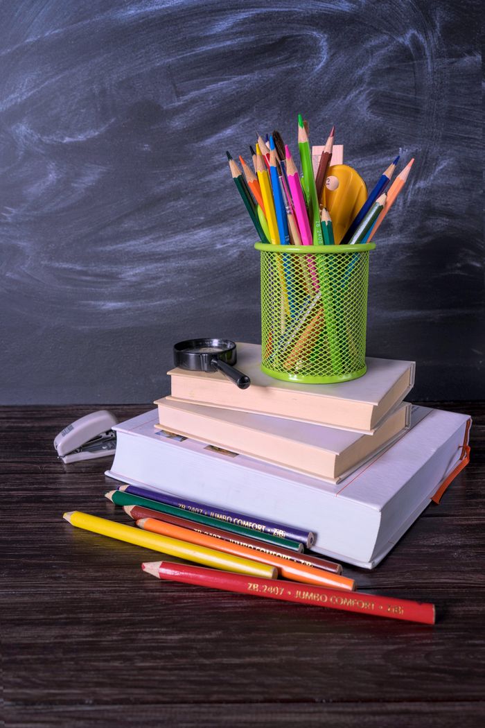 Pile of books and stationery on a desk with a chalkboard backdrop, ideal for educational themes.