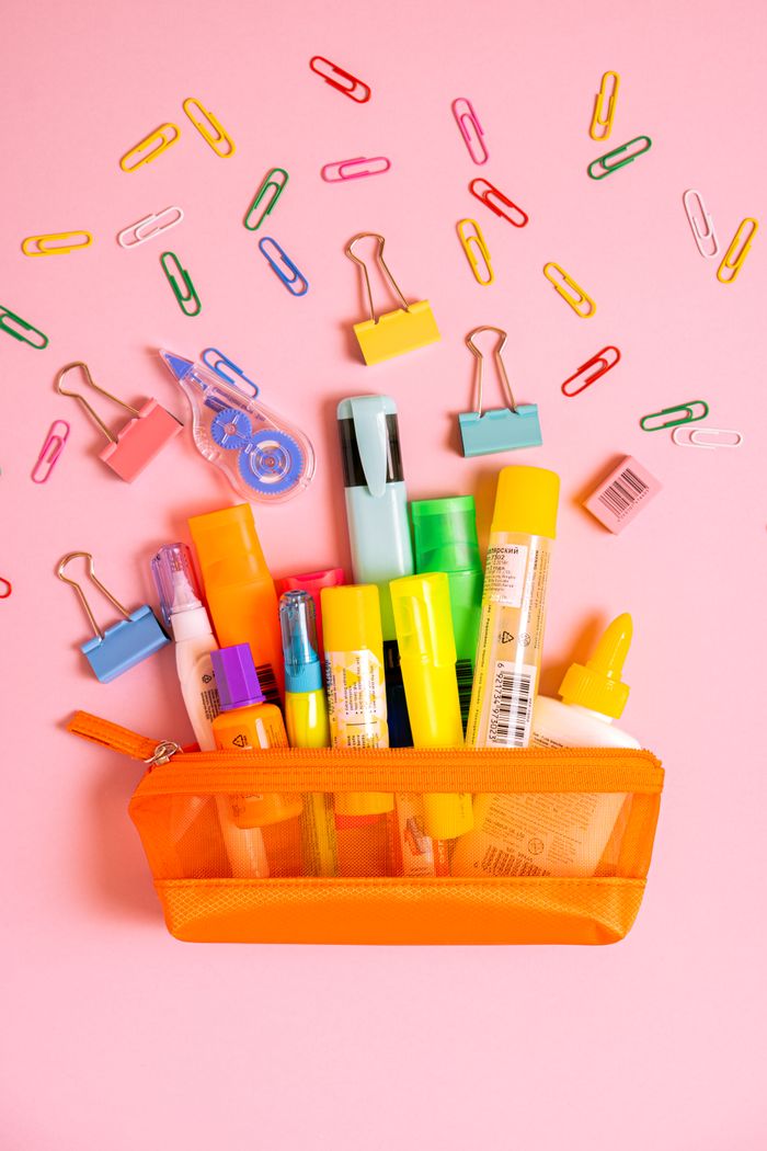 Vibrant desk supplies spilling from an orange pouch on a pink backdrop.